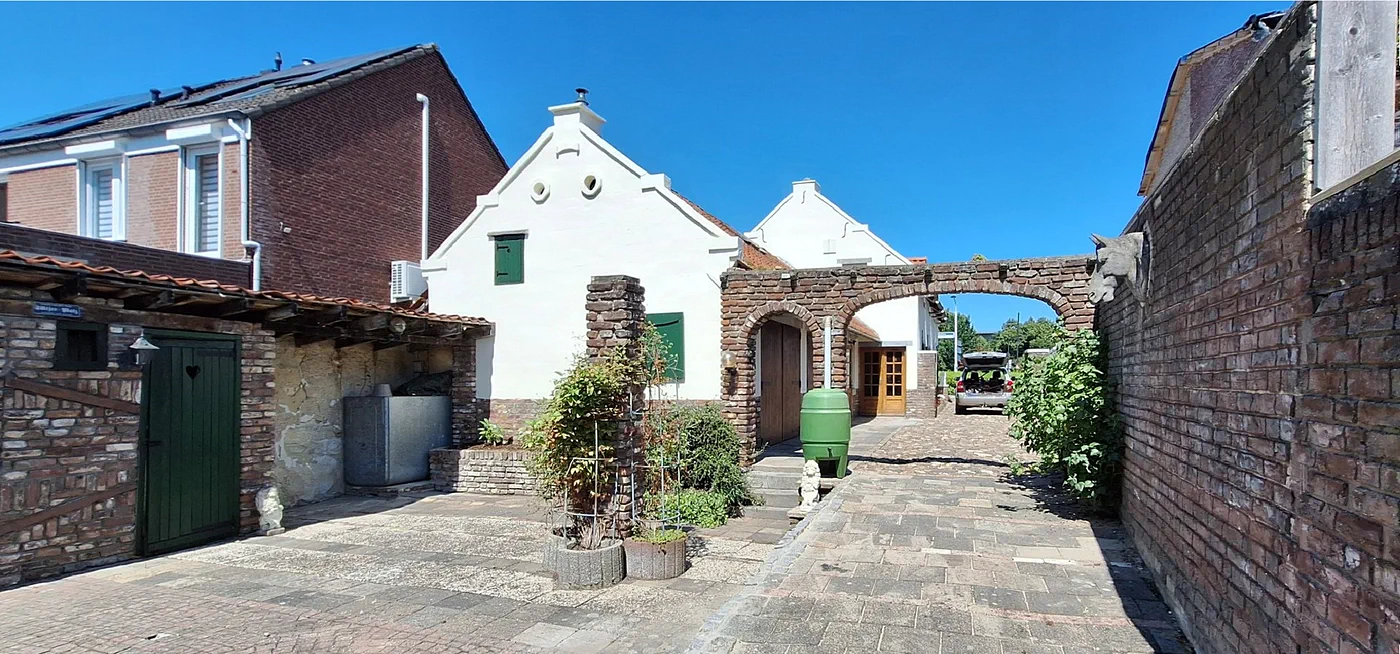 De binnenplaats achter het huis: twee witte puntgevels, een bakstenen boog en planten langs het pad