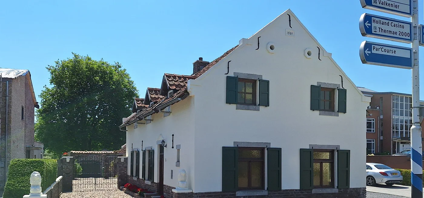 De voorkant van Bed and Breakfast 1691 op een zonnige dag: een wit huis met groene luiken, een bakstenen plint en het jaartal 1691 in de top van de gevel