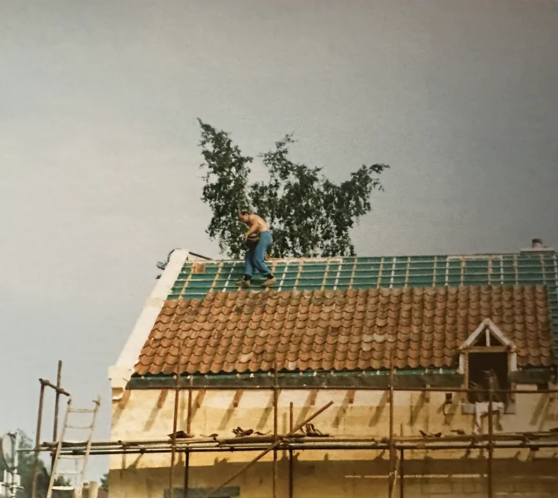 Iemand werkt bovenop het dak, met nieuwe rode pannen en een dakkapel, en een steiger langs de muur