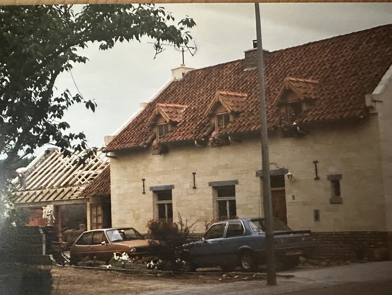 Het huis met de nieuwe gevel en dakkapellen, twee auto's van toen ervoor en het bijgebouw nog in de steigers