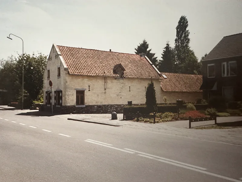 Het huis gezien vanaf de weg: de lange zijgevel van blanke mergel met het rode pannendak