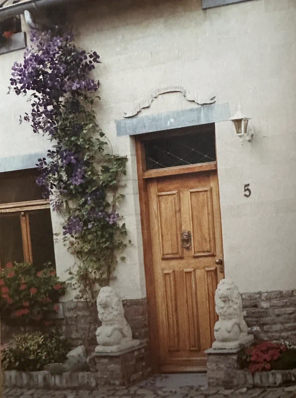 De houten voordeur met het huisnummer 5, twee stenen leeuwen en een paarse clematis