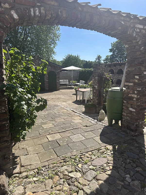 Een bakstenen boog in de tuinmuur, met daarachter het terras, de parasol en de groene deuren